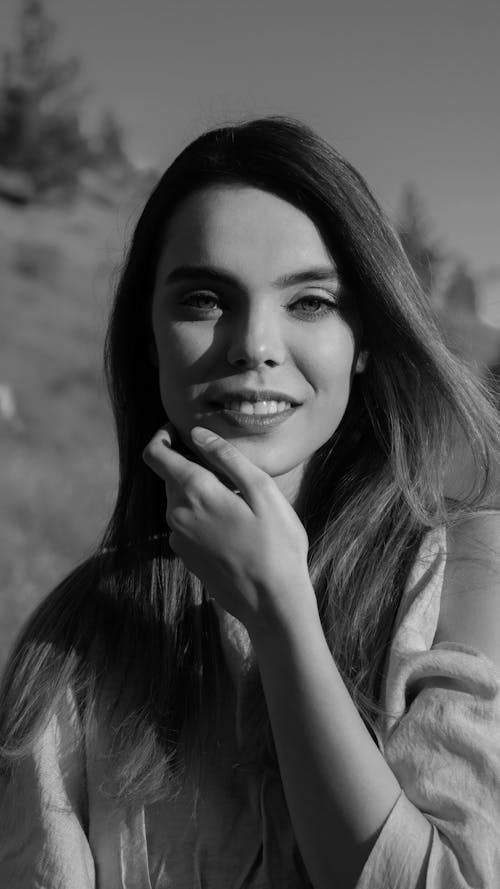 Black and white attractive happy female touching face gently and looking at camera with smile while standing in summer nature