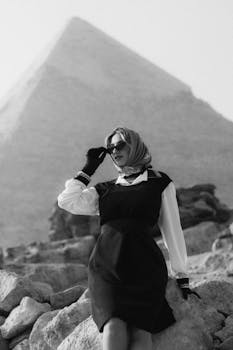 Elegant woman in vintage fashion poses by the Great Pyramid of Giza in a timeless monochrome scene.