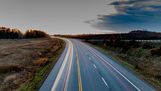 A picturesque highway at twilight showing light trails with a serene countryside backdrop.