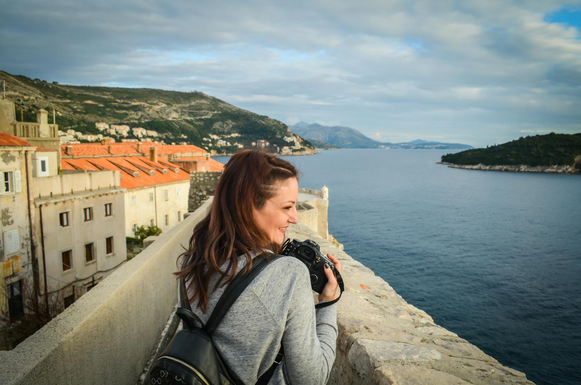 A woman photographs the stunning Dubrovnik coastline from ancient walls. Ideal for travel and architecture themes.