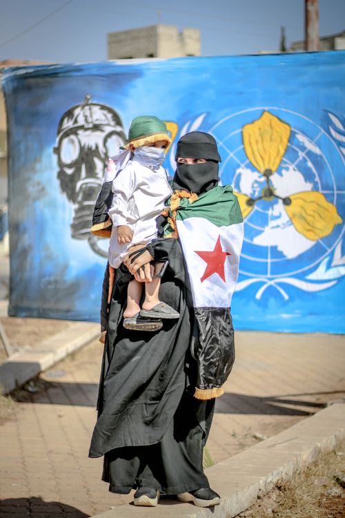 Free Full body of female in hijab wrapped in national flag standing with kid against graffiti wall Stock Photo