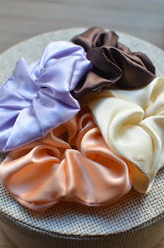 A bright and colorful collection of satin scrunchies displayed on a textured surface, offering a modern and elegant look.