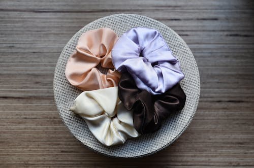 Overhead view of assorted silky hair bands on round shaped box on wooden table