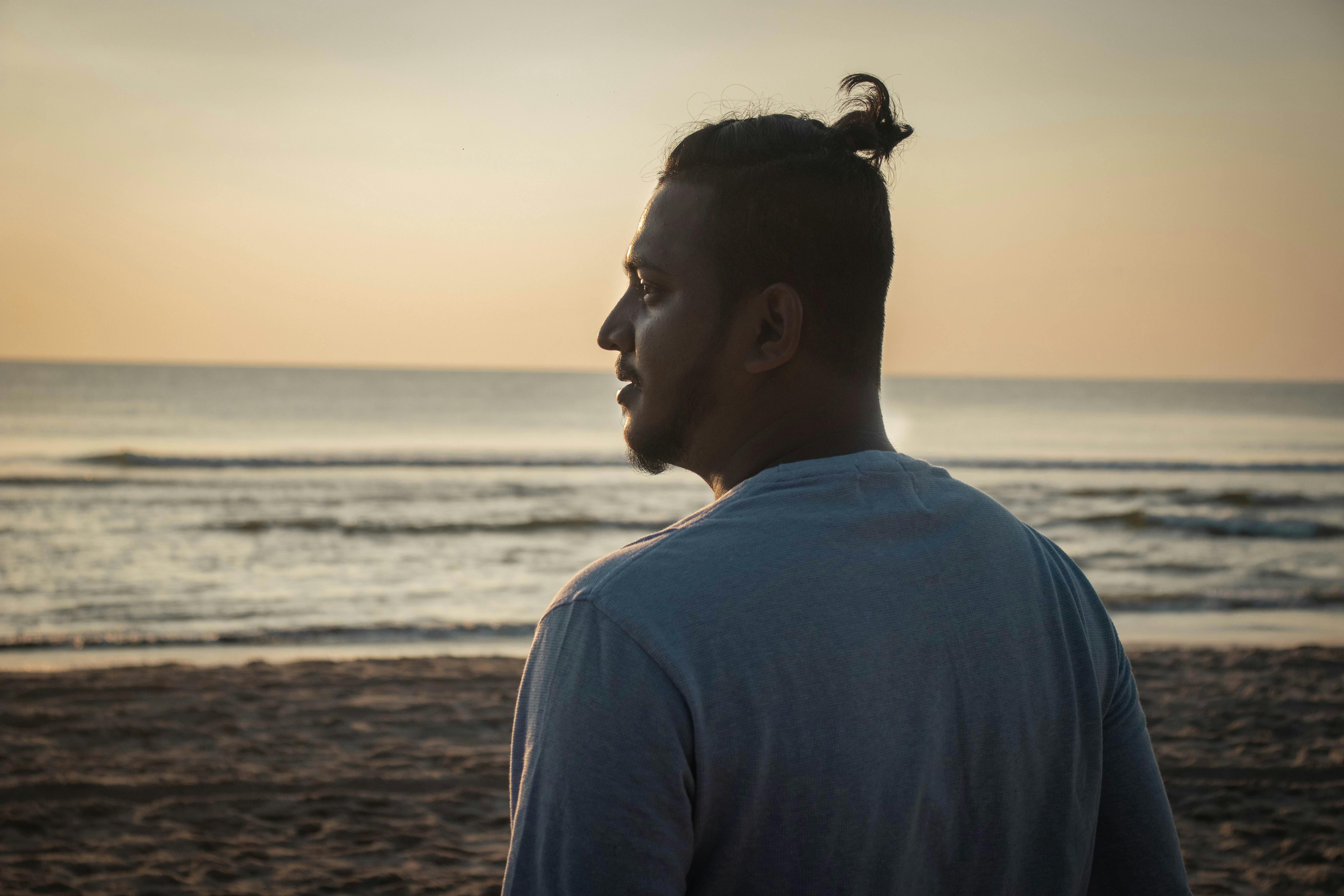 Profile of a man standing on a beach at sunset, looking thoughtfully at the sea.