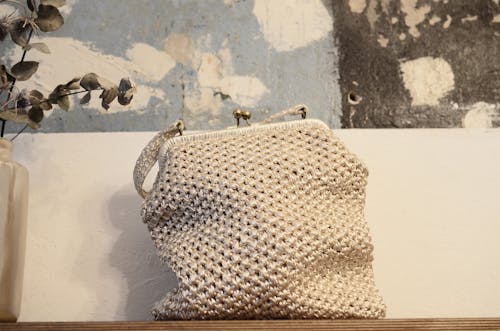 Organic knitted handbag with ornament and metal fastener on desk near rough wall in house