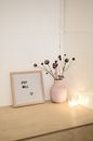 Wooden cabinet top with framed image with inscription Stay Well and dry plants in white vase near burning candle