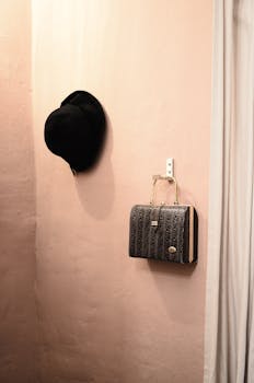 Fashionable black hat and handbag hanging on a minimalistic pink wall.