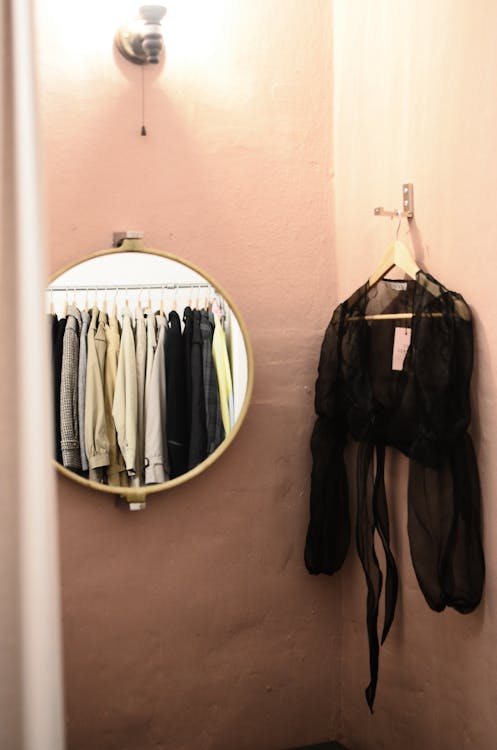 Free Interior of minimalistic room with lamp on wall and mirror with reflection of different clothes near blouse on hanger Stock Photo