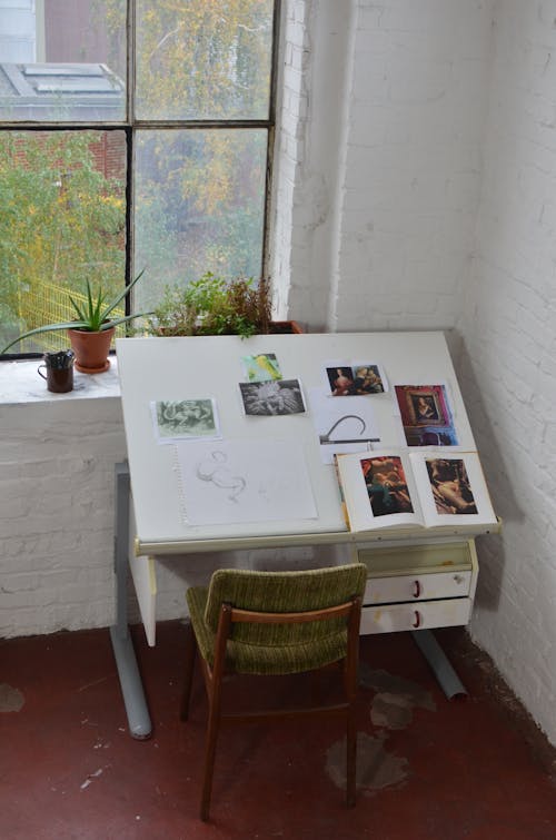 Interior of workplace with table for painter with different pictures and opened book in workshop