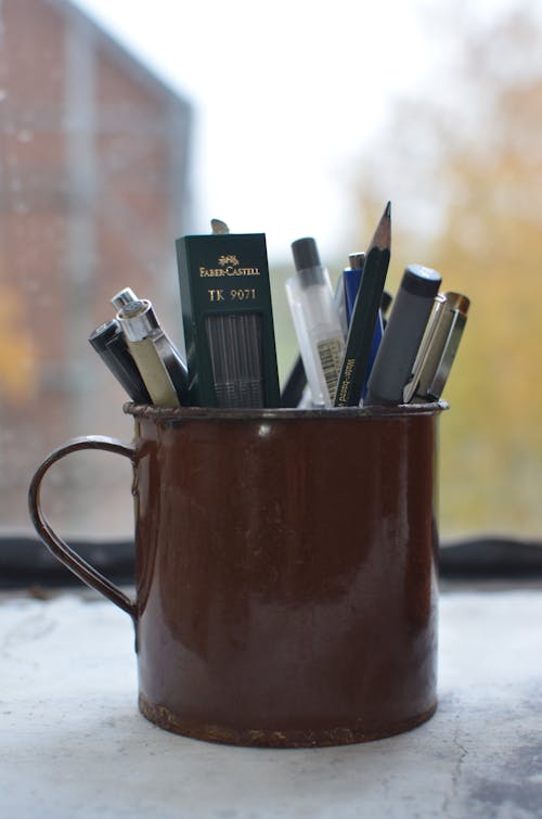 Cup with supply for writing and creating artworks placed on windowsill in workshop