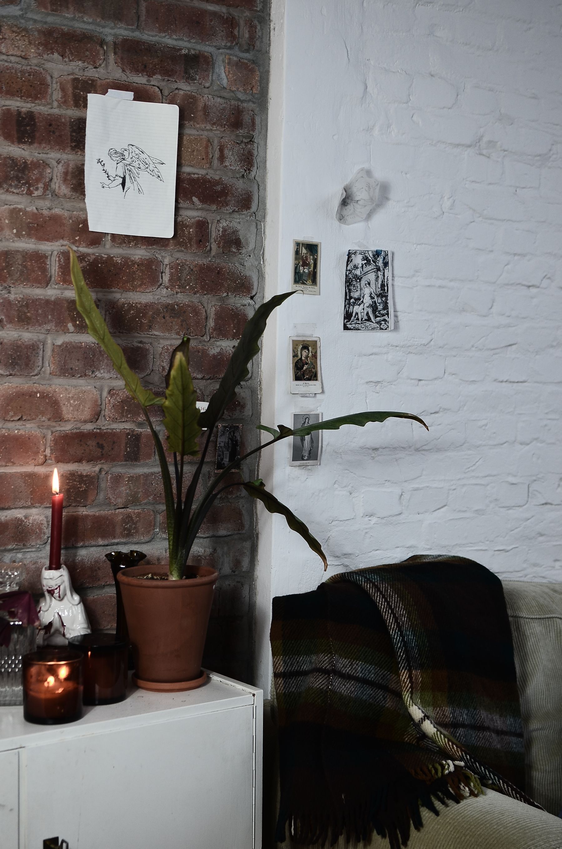 Sofa against rough brick with framed art, plants, blanket, sideboard and candlelight