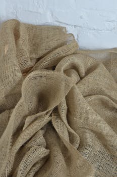 From above of creased organic sackcloth with tiny holes near whitewashed brick wall in daytime