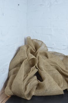 Creased burlap cloth on dark surface with whitewashed brick background, creating a rustic, minimalistic vibe.