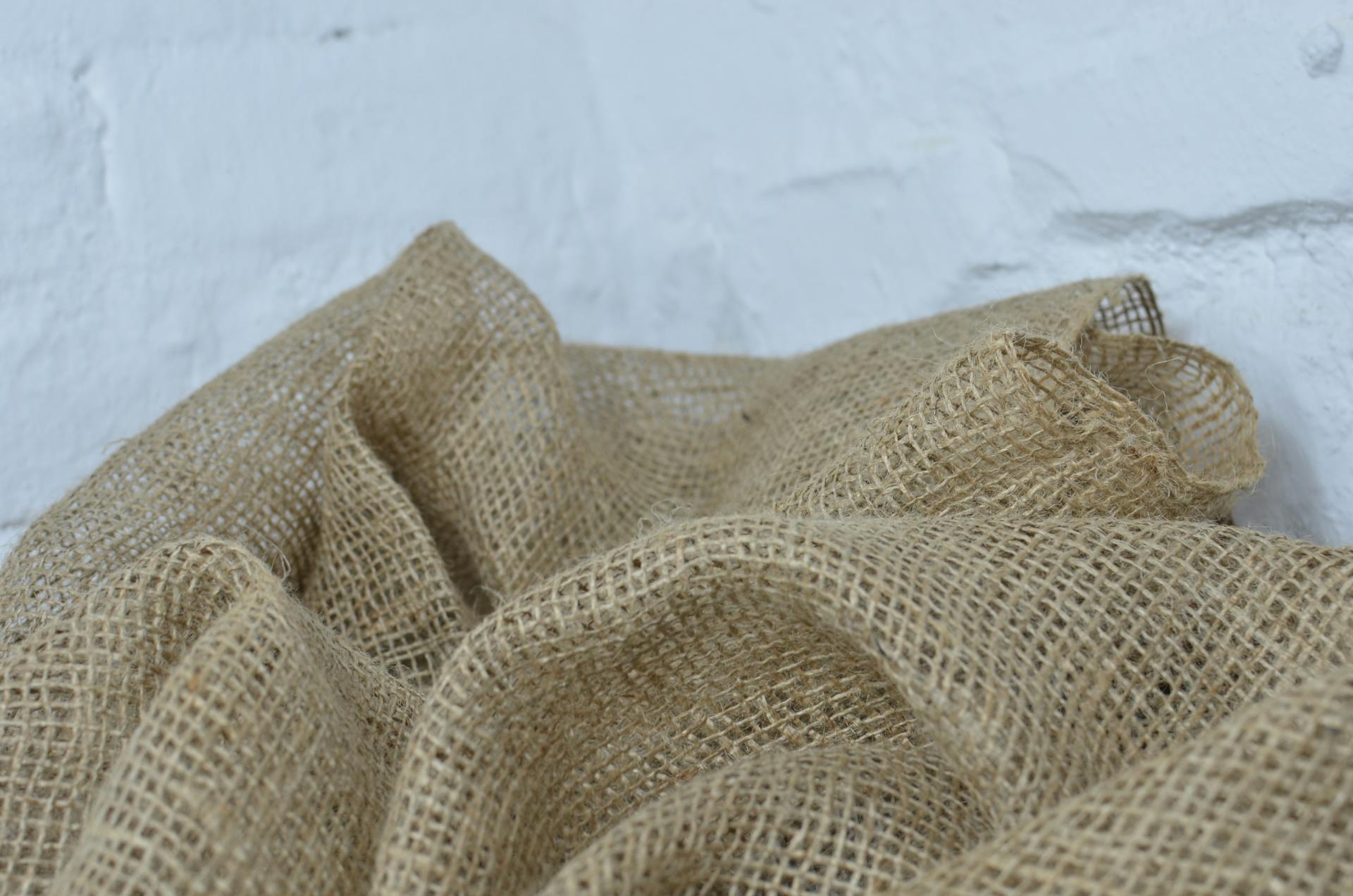 Close-up of eco-friendly burlap fabric against a white brick wall, showcasing texture and natural fibers.