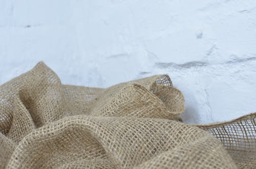 Closeup of creased organic burlap with tiny holes and thin fibers near rough white wall