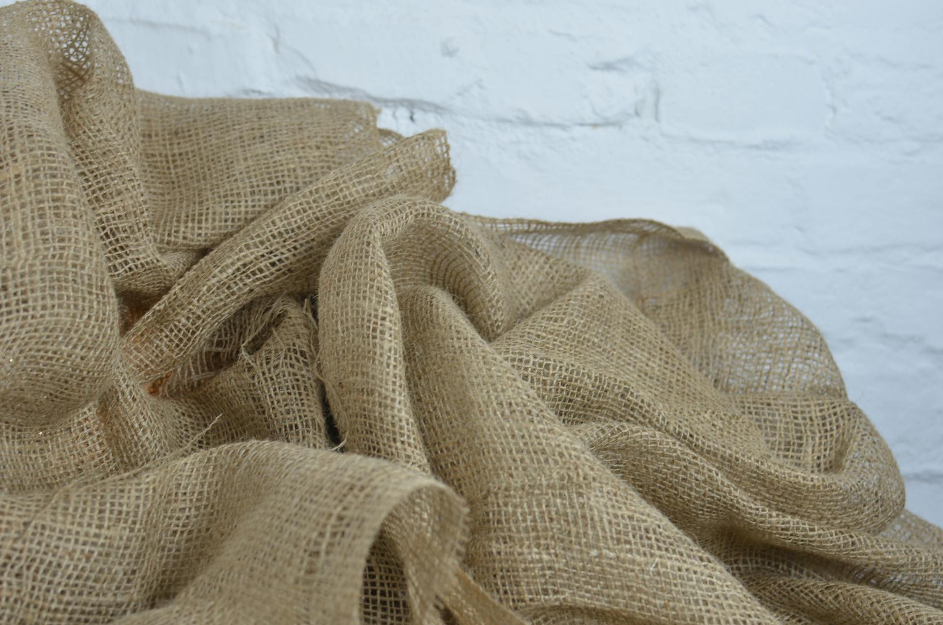 Textured burlap fabric draped with a white brick wall background, perfect for eco-friendly themes.
