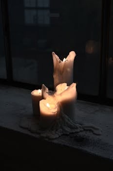 A group of melting candles casting a warm glow on a window sill in the evening darkness.