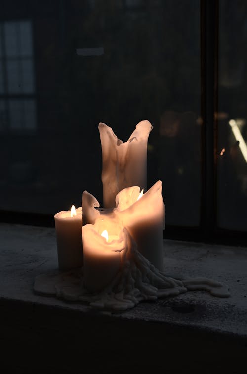 Shiny candles of different sizes with melted wax and hot flames at home in twilight