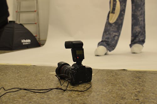 Professional modern photo camera with flash placed on floor in studio against crop faceless model