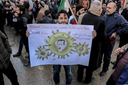 High angle of ethnic male activist with poster standing on crowded street at demonstration against policy