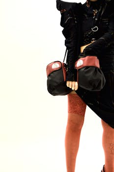 Crop anonymous female model wearing eccentric black outfit with vintage bag standing in studio against white background