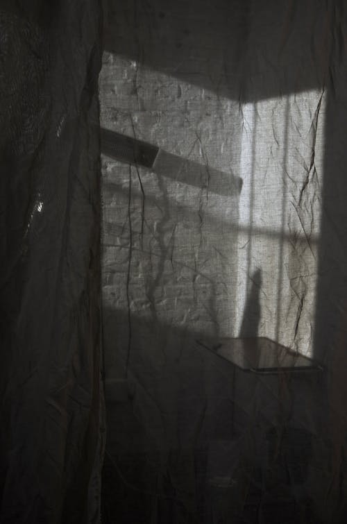 View through transparent crumpled curtain with table and lamp hanging on white brick wall