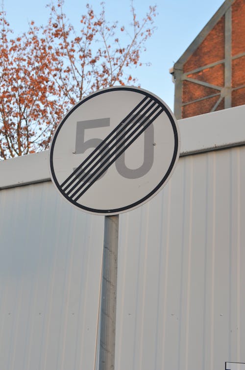 Speed limit end sign against fence in daylight