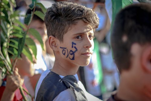 Side view of ethnic teenage boy with Arabic inscription on face standing on crowded street at protest movement against state policy