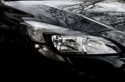 Polished reflecting surface of black modern car hood with glossy headlight on street