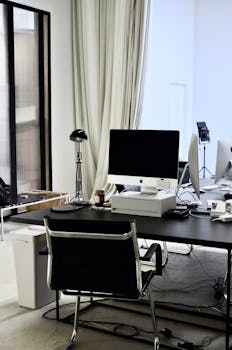 Modern workplace with convenient computer on black table and chair near wires on floor in office