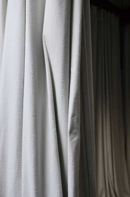 Crumpled fabric of curtains with creases hanging on wall in dark empty room