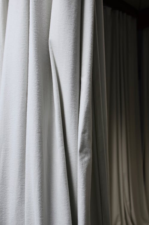 Crumpled fabric of curtains with creases hanging on wall in dark empty room