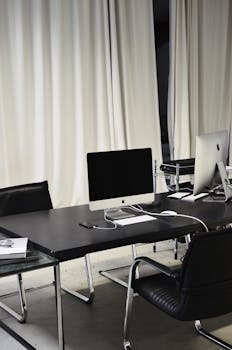 Black and white of computer with wireless keyboard and mouse placed on table near smartphone on charge in business office