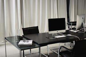 Black and white of workspace of office with computers placed on table with wireless mouse and keyboard near smartphone