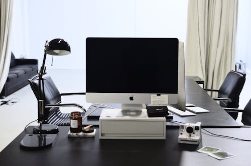 Monitor of modern computer placed on table near instant photo camera and lamp in contemporary workplace in daytime