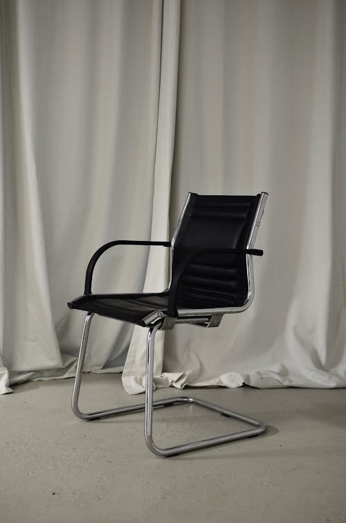 Black chair with leather seat and metal elements placed in light room against long curtain