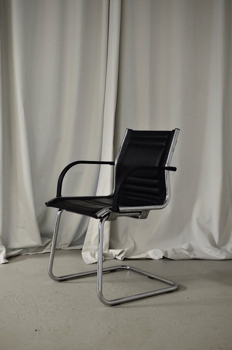 Black Chair Placed In Room Against Curtain