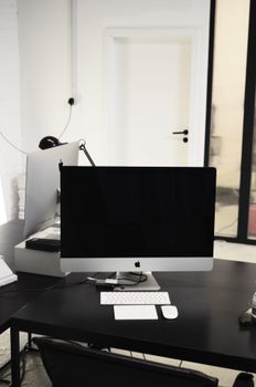 Interior of contemporary workspace with computer with black screen placed on black table with white keyboard and mouse