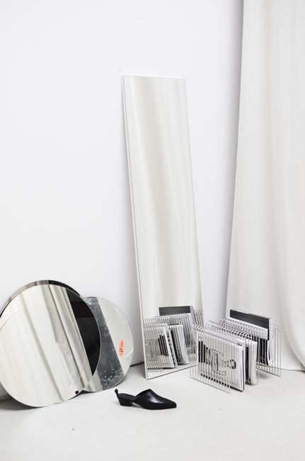 Different mirrors and books placed in room with light walls and floor in daytime