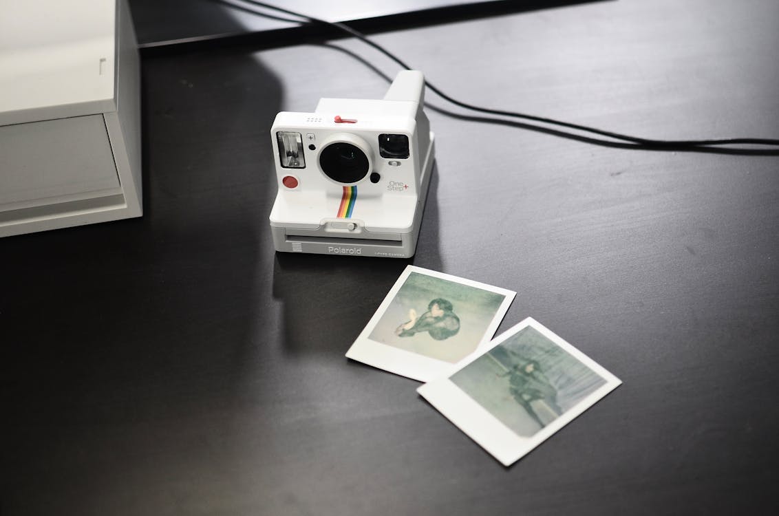 From above of contemporary photo camera with striped ornament near photos of woman on desk