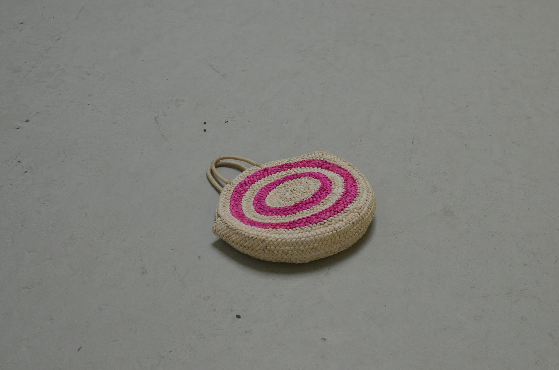 High angle of straw bag with bright round elements and handles on concrete surface