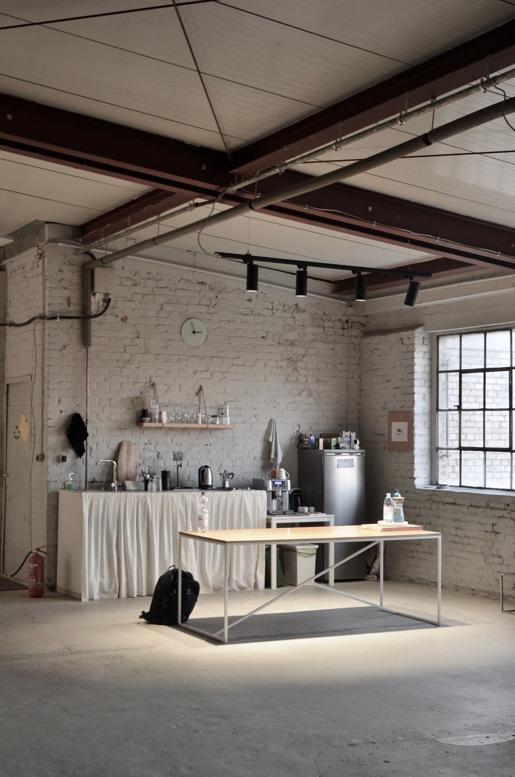 Loft kitchen with white brick, exposed beams, metal-framed table and fabric-covered base storage