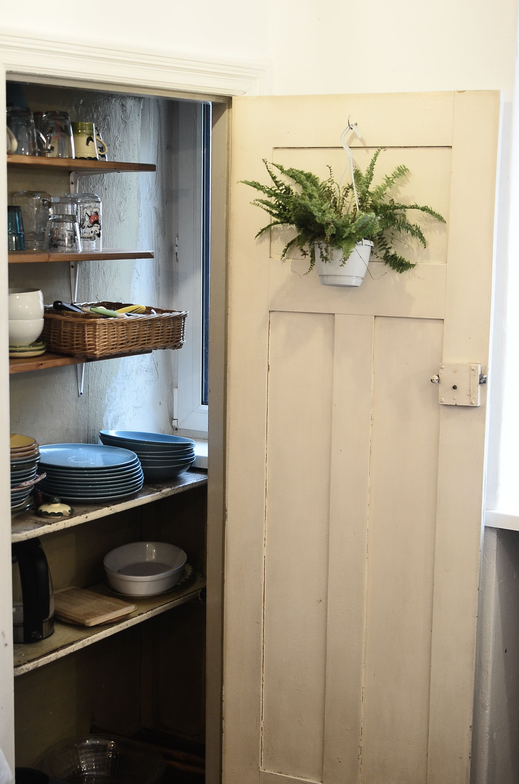 An open pantry cupboard with dishes, jars, a woven storage basket and clearly arranged shelving