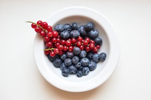 Top view of bowl with fresh blueberry and ripe red currant on table