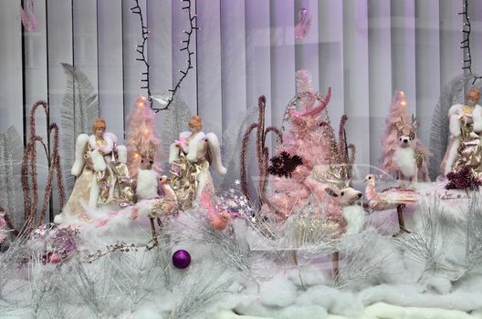 Through glass of dolls and toys on decorated showcase with snow and tree ball under garland
