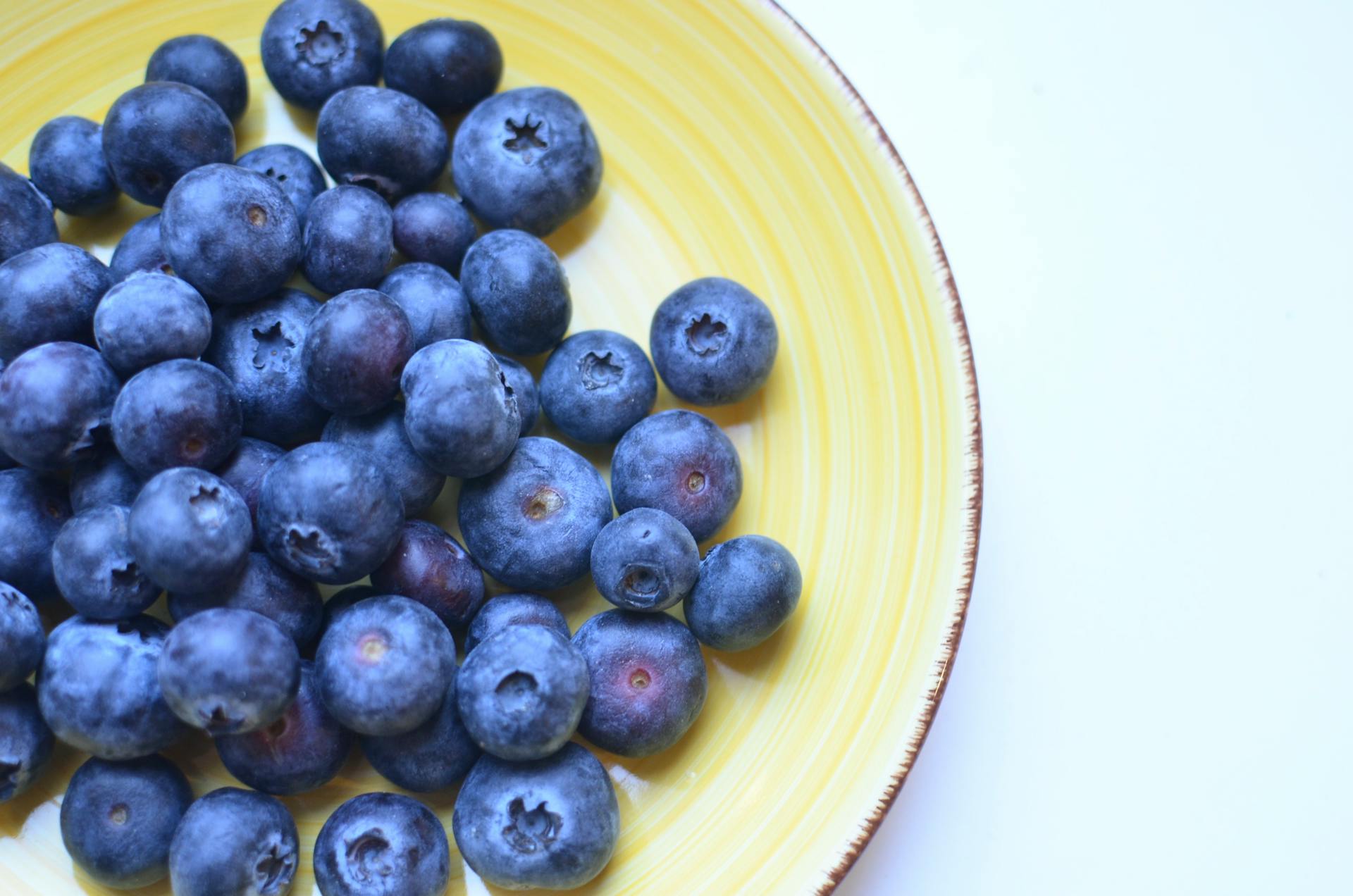 Top view of natural juicy blueberry with sweet taste on yellow ceramic plate