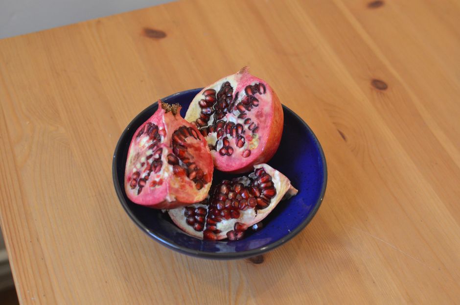 A pomegranate scored and split into sections with red arils being released into a glass bowl of water, seeds sinking to the bottom while white pith floats.