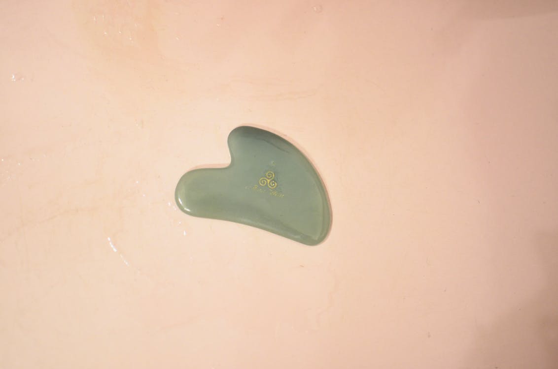 Top view of green shaped Gua Sha scraping massage tool placed in wet bathtub in bathroom during daily hygiene routine