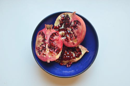 Top view of fresh ripe halves of pomegranate with red seeds in bowl placed on white background in light kitchen