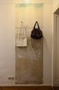White and dark feminine handbags hanging on hooks on shabby wall with sockets in light room near doorway at home